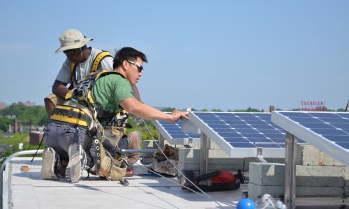 Two workers install solar panels on a roof