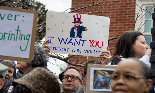 A person holds up a sign that reads "I want you to prevent gun violence"