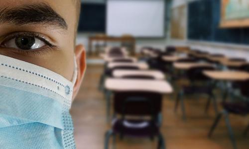 Student in an empty classroom wears a mask.