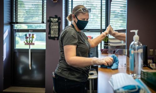 A masked school teacher, wiping down her classroom.