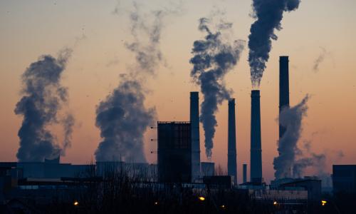 The silhouette of a factory emitting smoke.