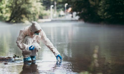 A scientist taking a water sample from a flooded area.