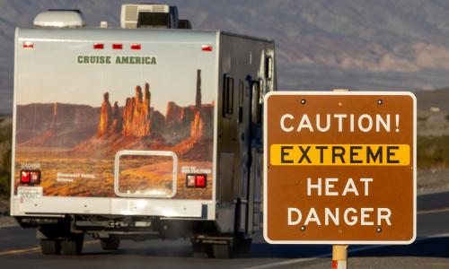 An RV drives past a sign that reads "Caution! Extreme heat danger."