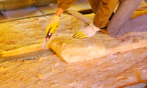 Person cutting insulation material in an attic.